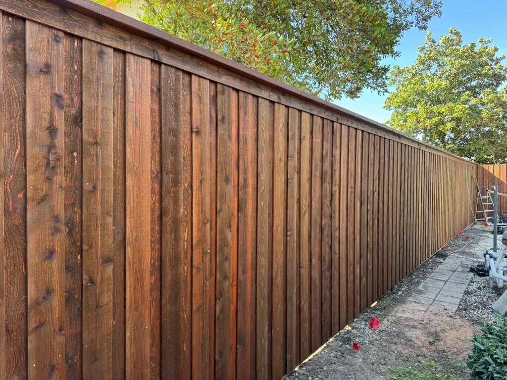 Dark stained cedar privacy fence showing vertical pickets and a finished top cap