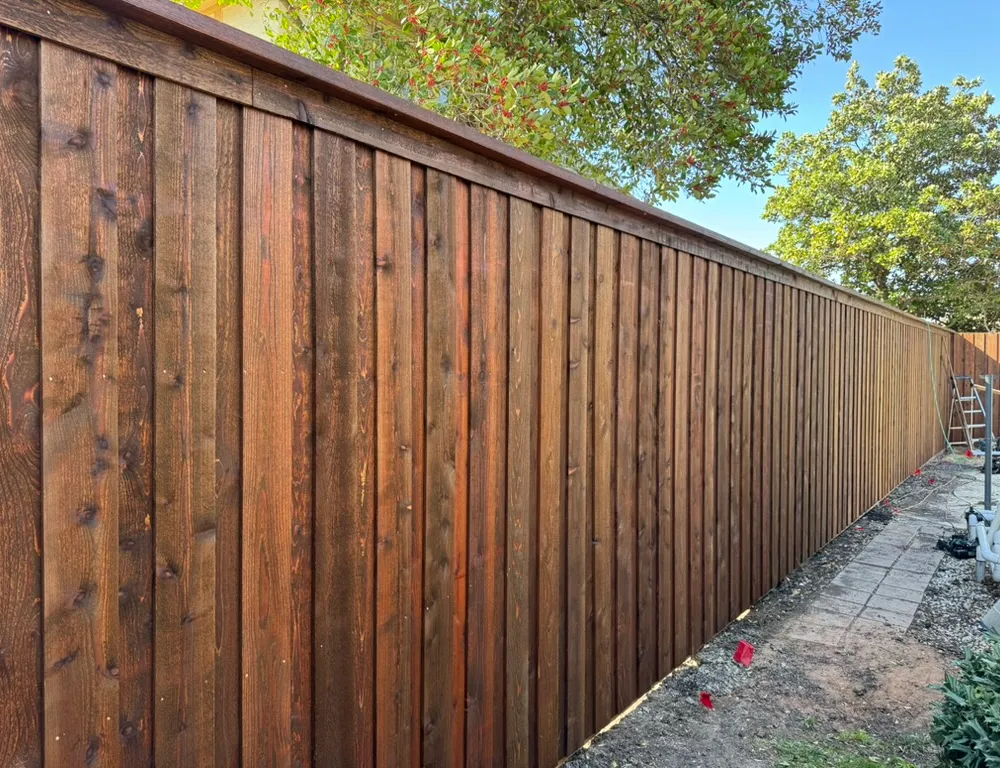 Dark stained cedar privacy fence showing vertical pickets and a finished top cap