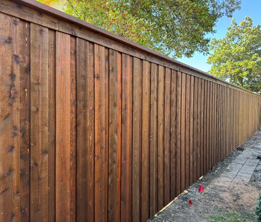 Dark stained cedar privacy fence showing vertical pickets and a finished top cap