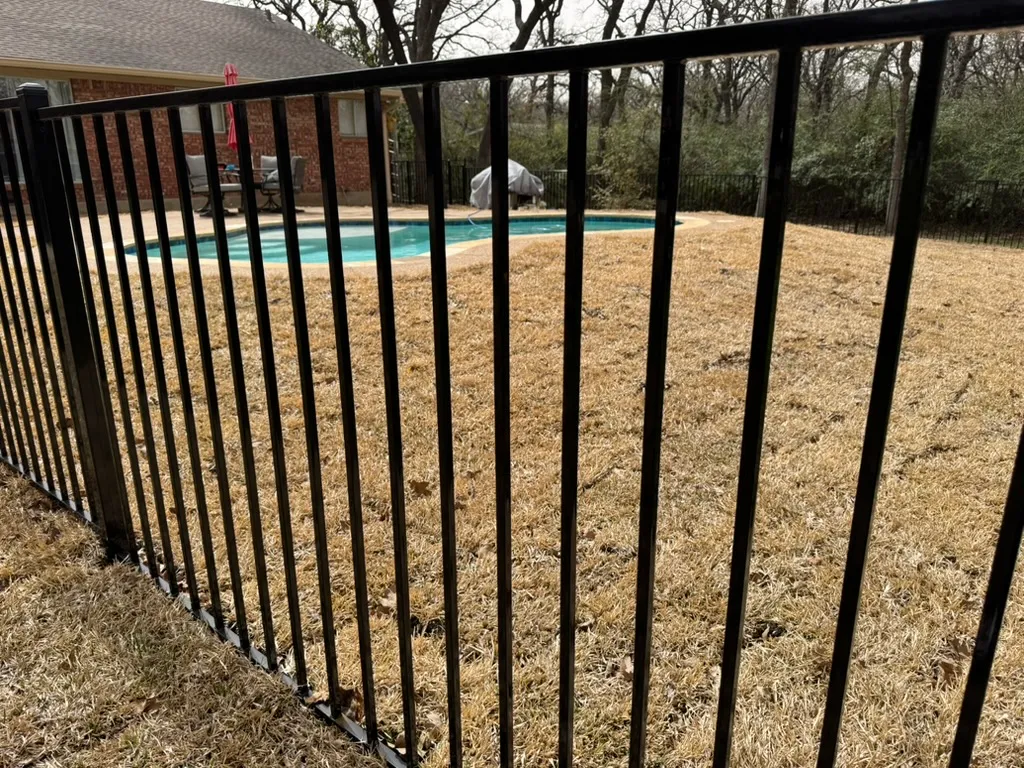 Black ornamental metal pool barrier enclosing a backyard swimming pool